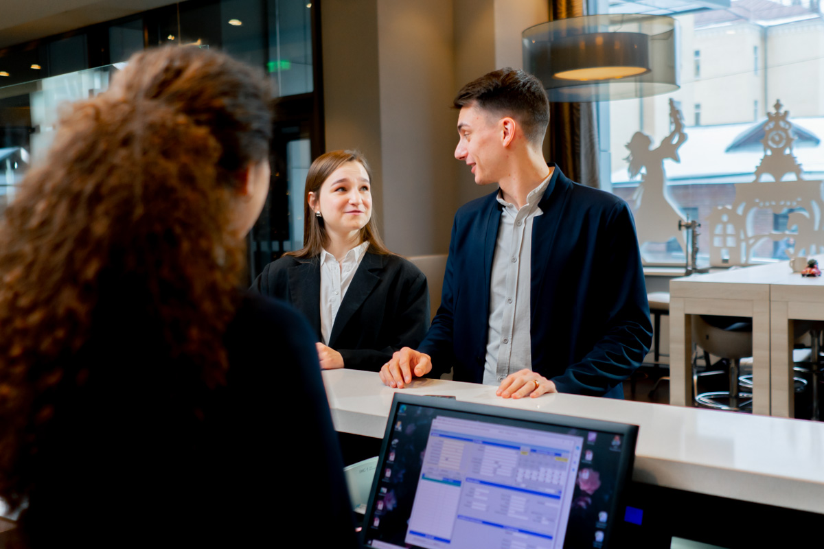 The Receptionist At The Counter Meets Guests With Luggage In The