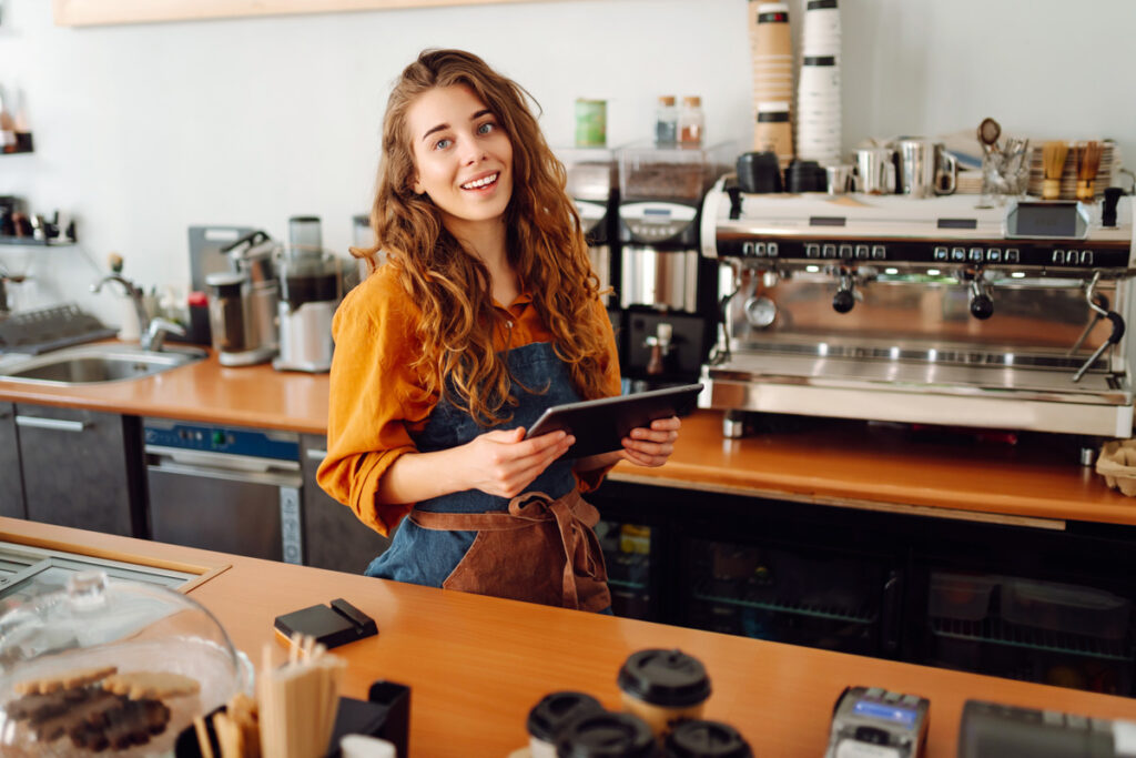 Smiling Female Barista Takes An Order From A Tablet While Standing At Bar Counter In A Coffee Shop.